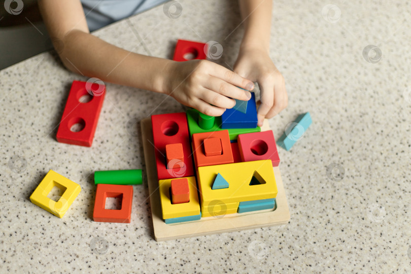 Скачать Ребенок играет с развивающей игрушкой-головоломкой, изготовленной из экологически чистого древесного материала фотосток Ozero