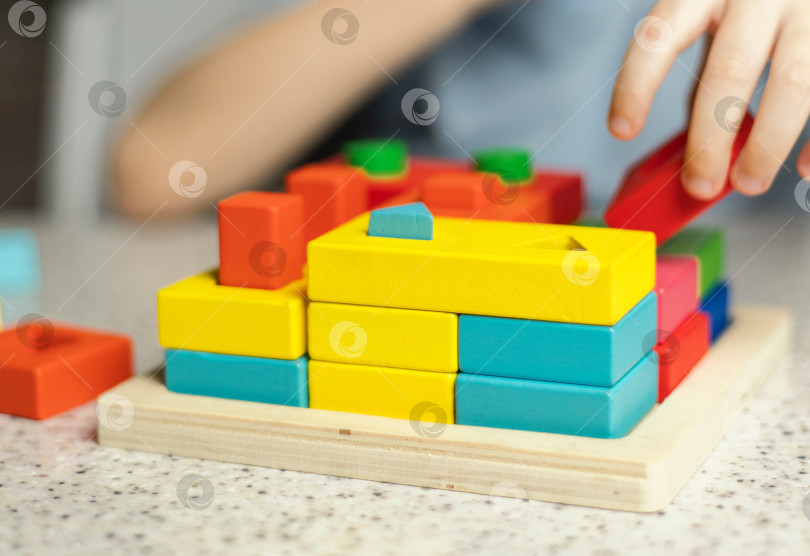 Скачать Крупный план детских рук, играющих с развивающей разноцветной игрушкой-головоломкой, изготовленной из экологически чистого древесного материала фотосток Ozero