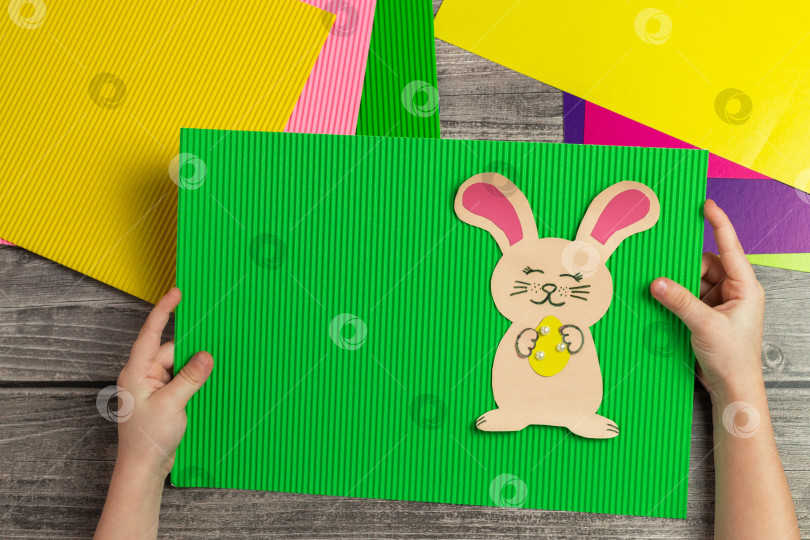 Скачать Ребенок своими руками делает открытку с пасхальным кроликом. Аппликация из разноцветной бумаги. Поделка пасхального кролика фотосток Ozero