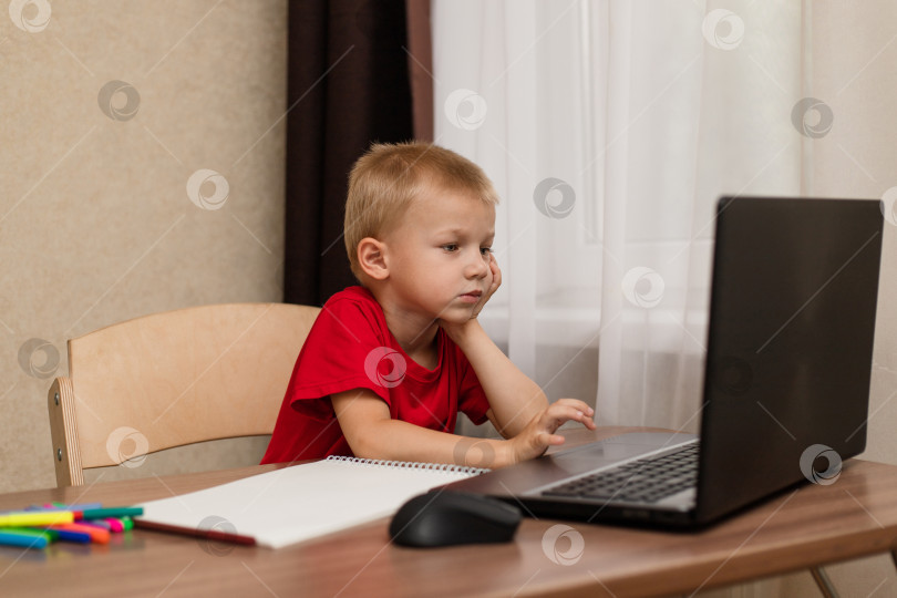 Скачать Дистанционное онлайн-обучение. Ребенок внимательно смотрит в ноутбук и изучает урок рисования онлайн в Интернете. Онлайн-школа. фотосток Ozero