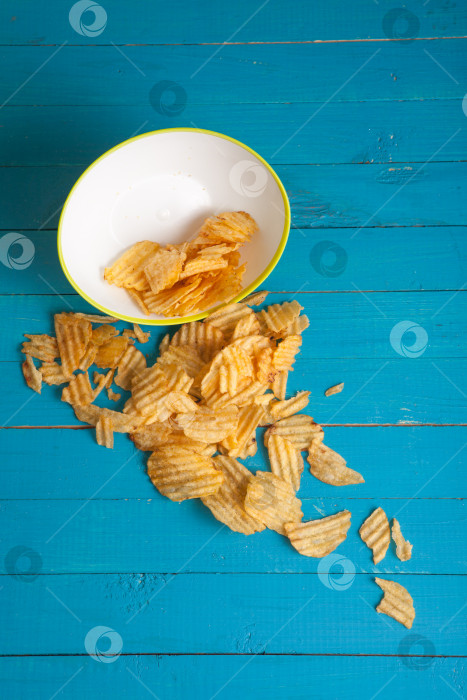 Скачать Картофельные чипсы высыпались из тарелки на синий деревянный стол фотосток Ozero