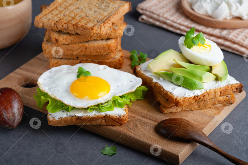 Скачать Бутерброды с творожным сыром, жареным яйцом, авокадо и зеленью фотосток Ozero