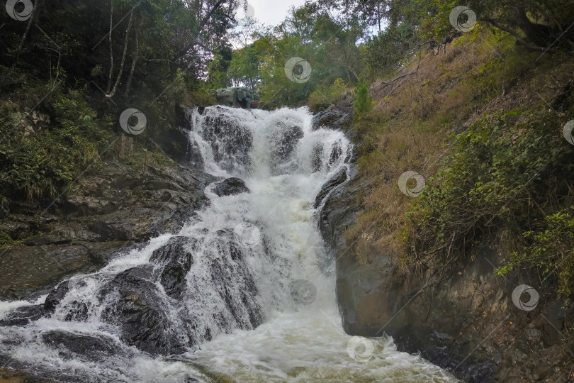 Скачать Между горными склонами бушует водопад, пенясь на камнях. фотосток Ozero