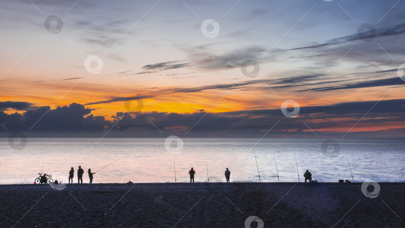 Скачать После захода солнца. На берегу моря видны силуэты людей и удочки для ловли рыбы фотосток Ozero