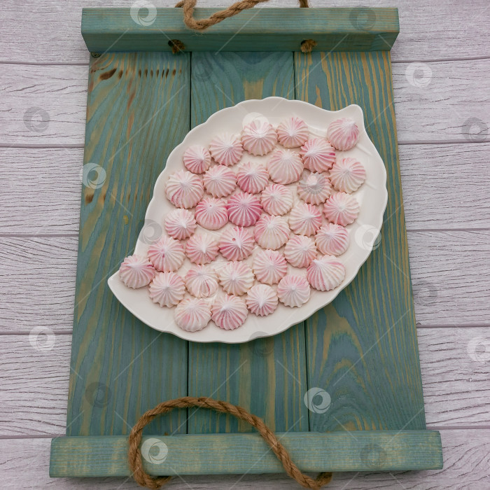 Скачать Маленькие бледно-розовые меренги для украшения выпечки выкладываются на белую тарелку в форме листа. = фотосток Ozero