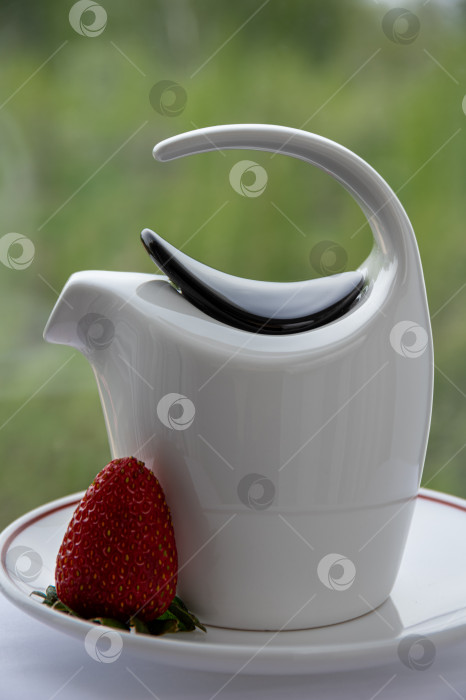 Скачать Изящный белый фарфоровый чайник на блюдце с клубникой. фотосток Ozero