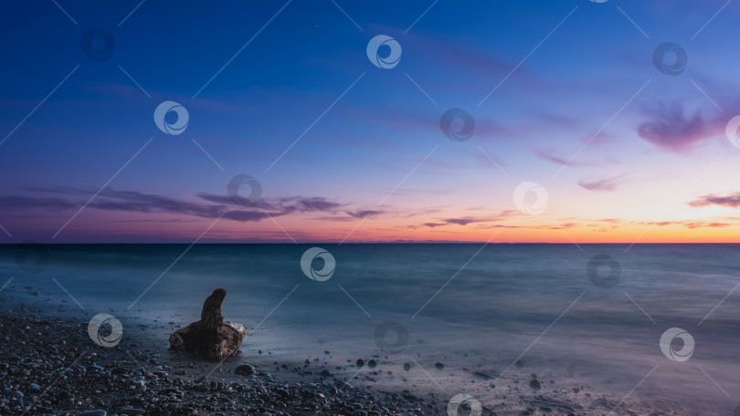 Скачать Сумерки после захода солнца.Спокойное бирюзовое море. На галечном пляже лежит старое живописное бревно фотосток Ozero