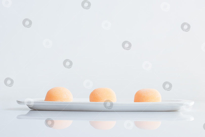 Скачать Три апельсиновых коржа, выложенных в ряд на белой тарелке.  Традиционный японский десерт Дайфуку моти. фотосток Ozero