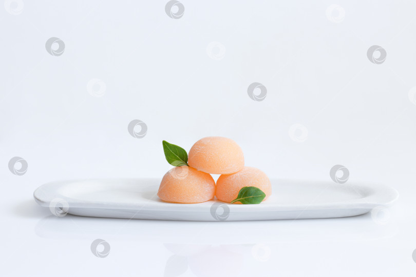 Скачать Три апельсиновых коржа, украшенных маленькими листочками, на белой тарелке. Десерт Дайфуку моти. фотосток Ozero