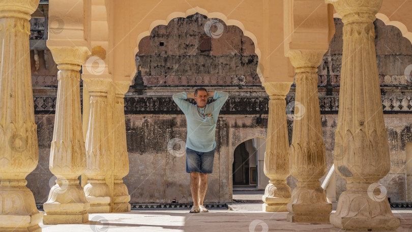 Скачать Павильон во внутреннем дворе дворца. Между резными колоннами, под аркой, стоит мужчина. фотосток Ozero