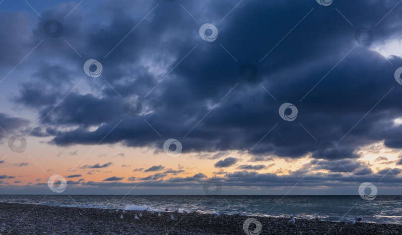 Скачать Вечернее небо затянуто темно-синими облаками.  Морские волны, пенящиеся на пляже. фотосток Ozero