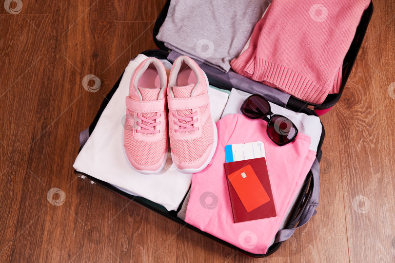Скачать Открытый чемодан с одеждой, кроссовками, солнцезащитными очками. Паспорт, карточка, билеты на поездку. фотосток Ozero