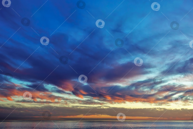 Скачать Яркий закат над морем. На вечернем небе голубые облака выделяются алым и оранжевым цветами. фотосток Ozero
