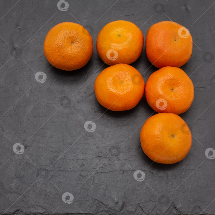 Скачать Яркие спелые мандарины лежат на черной сервировочной плитке. фотосток Ozero