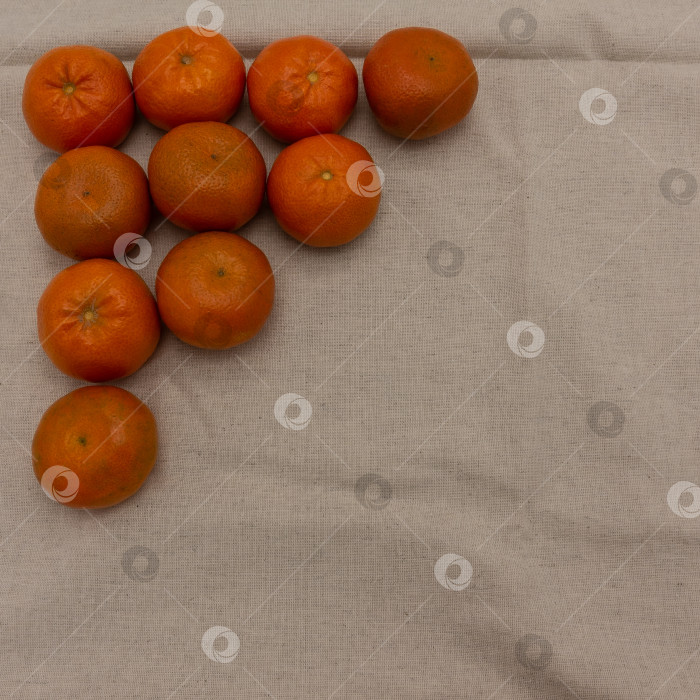 Скачать Спелые мандарины лежат на бежевой салфетке. Плоды выкладываются в форме треугольника фотосток Ozero
