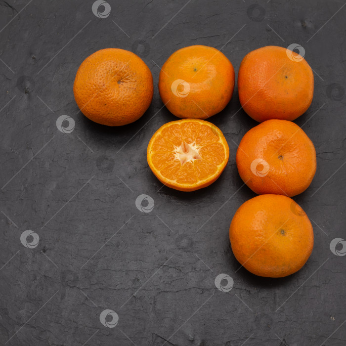 Скачать Яркие спелые мандарины на сервировочной плитке из черного камня. Пять целых плодов и одна половинка. фотосток Ozero