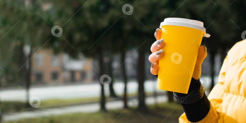 Скачать Женская рука, держащая желтую одноразовую чашку кофе крупным планом, снаружи. Женщина в ярко-желтом жакете, с блестящим маникюром. Баннер, скопируйте место для вашего текста фотосток Ozero