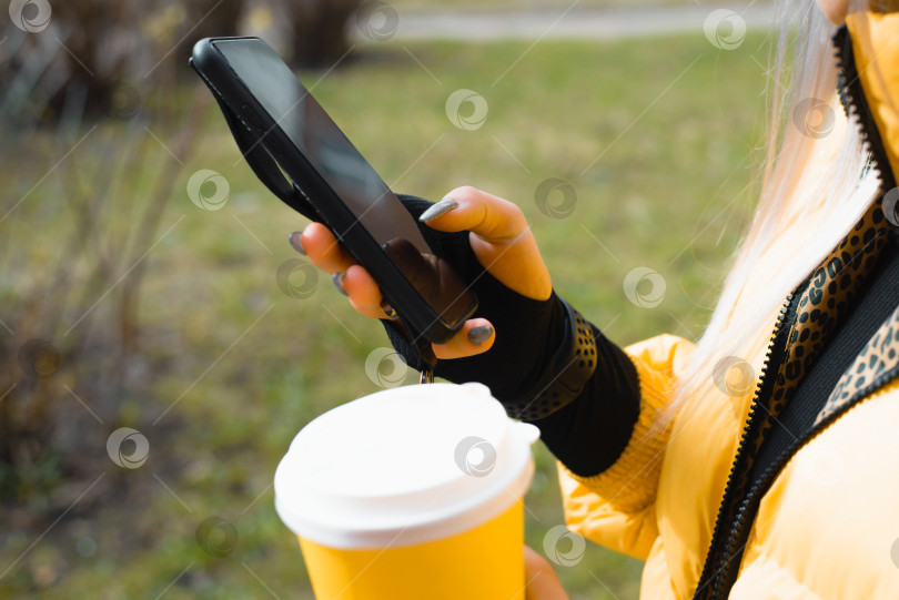 Скачать Крупный план женских рук, пользующихся смартфоном и держащих чашку кофе на улице. Избирательный фокус. фотосток Ozero