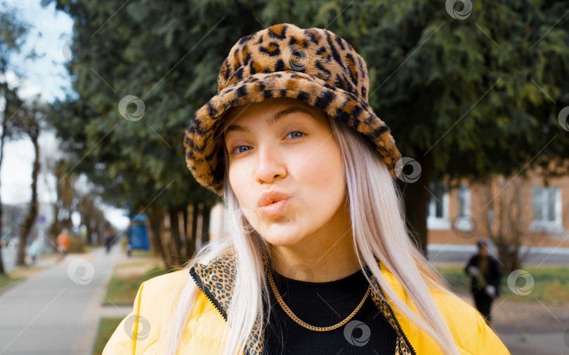 Скачать Портрет молодой женщины-хипстера в леопардовой шляпе, целующейся перед камерой на улице фотосток Ozero