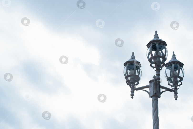 Скачать Винтажный фонарь на улице, на фоне пасмурного неба. Три лампы на декоративном столбе. Пространство для копирования фотосток Ozero