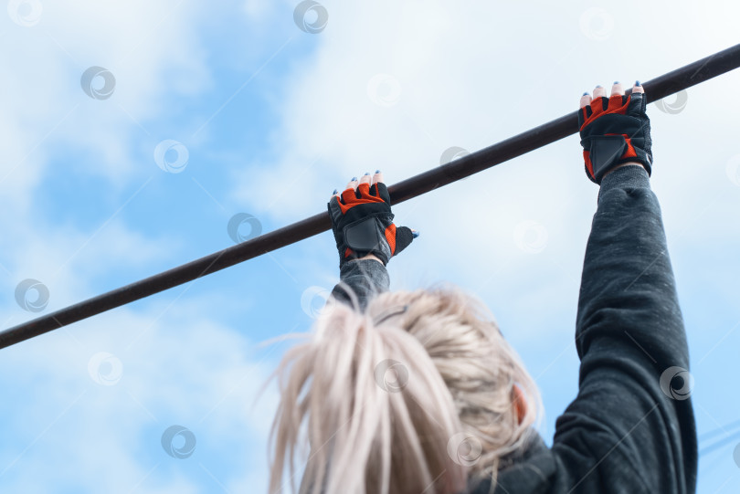 Скачать Женщина в спортивных перчатках тренируется подтягиваться на турнике. Тренировка на открытом воздухе. Активный образ жизни фотосток Ozero