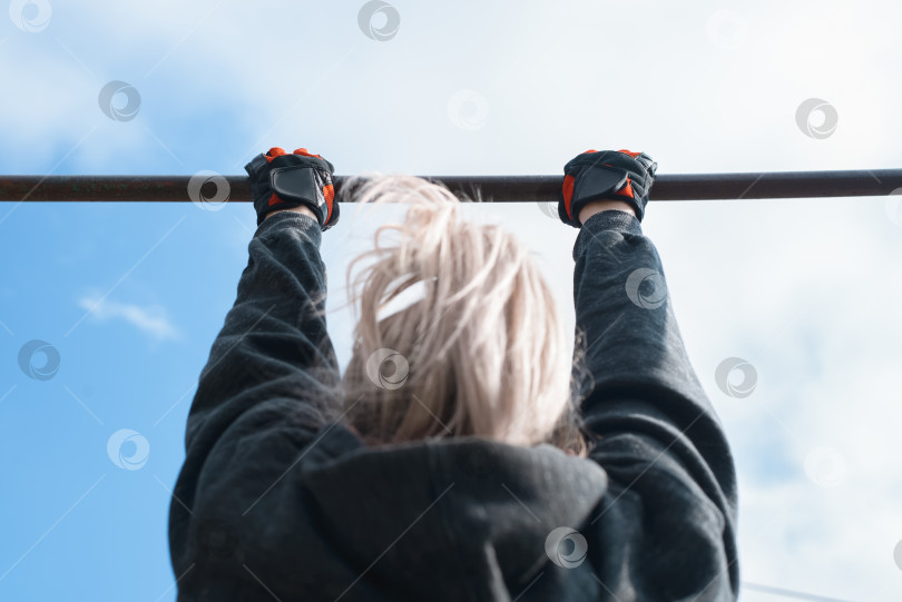 Скачать Женщина тренируется подтягиваться на турнике снаружи. Тренировка на открытом воздухе. Активный образ жизни. Вид сзади, сосредоточьтесь на руках фотосток Ozero