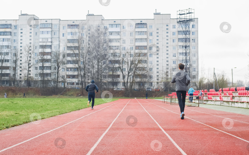 Скачать Спортсмены-любители-бегуны на стадионе снаружи, вид сзади. Люди, тренирующиеся на свежем воздухе, ведут активный образ жизни. фотосток Ozero