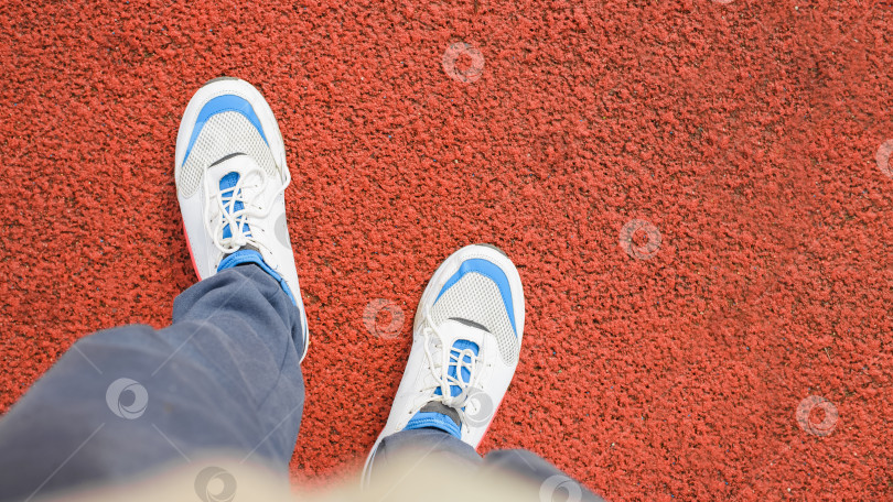 Скачать Спортсмен стоит на прорезиненном красном покрытии снаружи. Ноги в спортивных кроссовках крупным планом, вид сверху. Активный образ жизни, концепция тренировок фотосток Ozero
