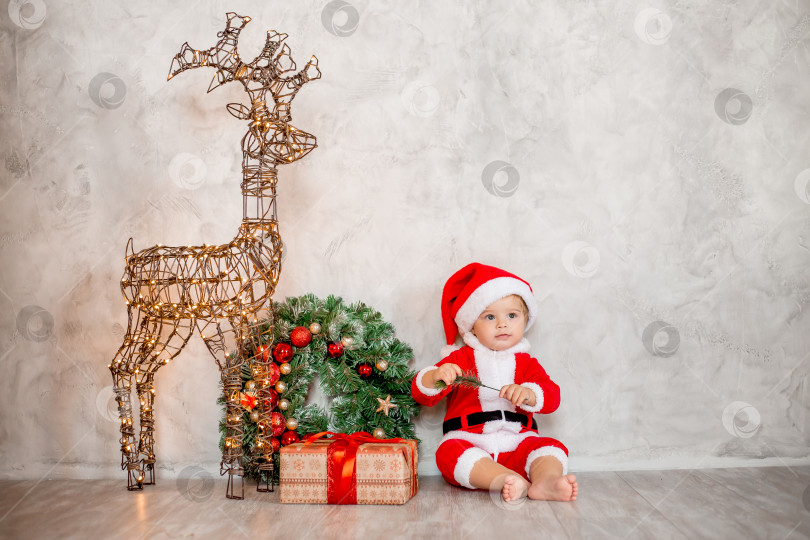 Скачать Милый малыш Санта сидит на деревянном полу с подарком и рождественским венком. Рождественская концепция, текстовое пространство фотосток Ozero