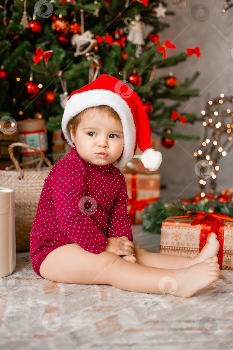 Скачать Милый малыш Санта сидит дома возле рождественской елки с подарками фотосток Ozero