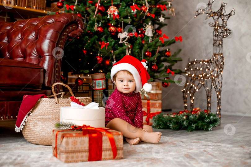 Скачать Милый малыш Санта сидит дома возле рождественской елки с подарками фотосток Ozero