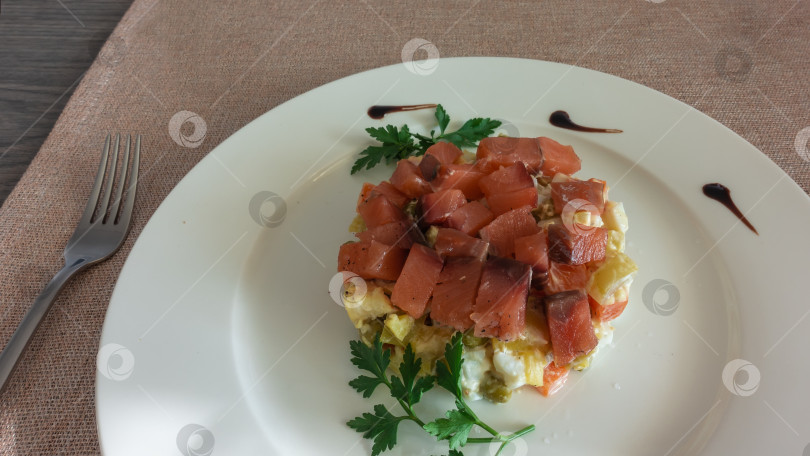 Скачать Салат из лосося с картофелем выкладывают на белую тарелку. Украшение - веточки петрушки, капли соуса. фотосток Ozero