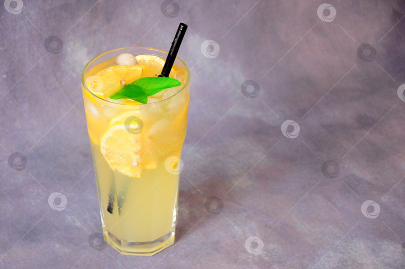 Скачать Высокий бокал лимонного мохито со льдом, ломтиками лимона и листьями мяты стоит на сером фоне. фотосток Ozero