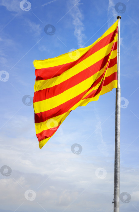 Скачать Флаг Каталонии на фоне голубого неба с облаками. фотосток Ozero