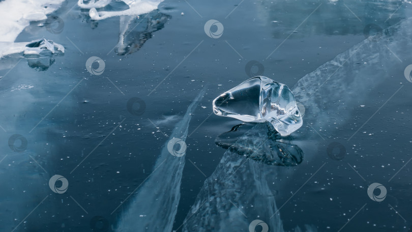 Скачать Прозрачный кусок льда причудливой формы лежит на толстом синем льду с трещинами. фотосток Ozero