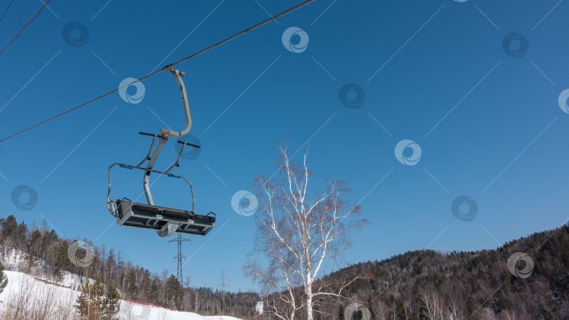 Скачать Пустая кабина кресельного подъемника на тросе на фоне голубого неба. фотосток Ozero