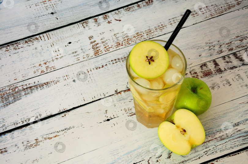 Скачать На деревянном столе стоит стакан яблочного сока со льдом и ломтиками фруктов. фотосток Ozero