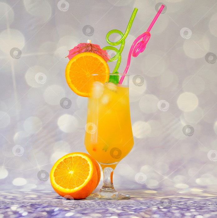 Скачать Высокий стакан апельсинового сока со льдом, украшенный ломтиком фрукта, соломинками и зонтиком на сером блестящем фоне. фотосток Ozero