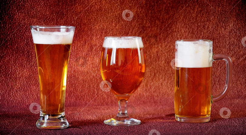 Скачать Высокий стакан, кружка с ручкой и стакан, полный светлого пива с белой пеной, стоят в ряд на коричневом абстрактном фоне. фотосток Ozero