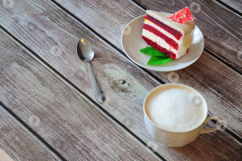 Скачать На деревянном столе стоит чашка свежего черного кофе, десертная ложка и тарелка с кусочком торта "красный бархат", украшенного листиками мяты. фотосток Ozero