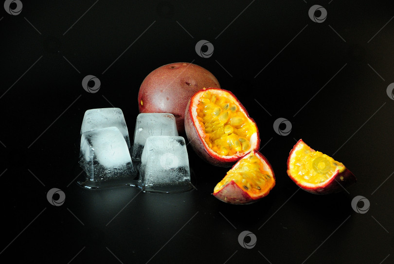 Скачать Маракуйя, спелый экзотический фрукт с кубиками льда на черном фоне. фотосток Ozero