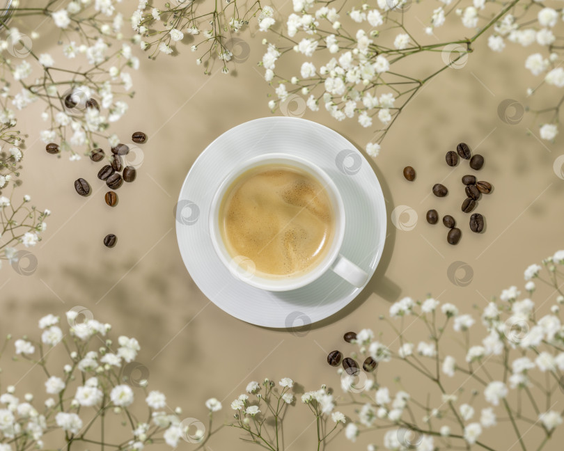 Скачать Чашка натурального кофе и кофейные зерна на бежевом фоне с белыми цветами фотосток Ozero