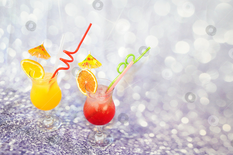 Скачать Два бокала цитрусовых соков со льдом и соломинками, украшенные дольками апельсина и грейпфрута на сером фоне. фотосток Ozero