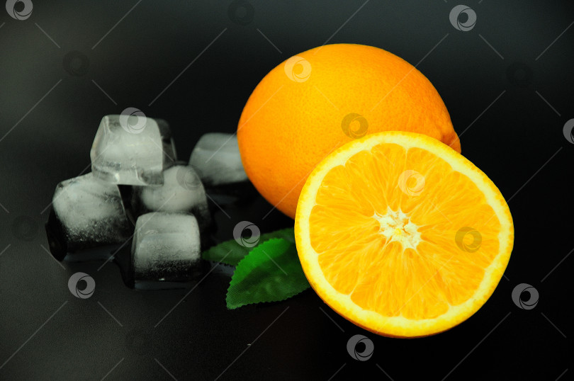 Скачать Два спелых апельсина с листьями и кусочками растаявшего льда лежат на черном фоне. фотосток Ozero