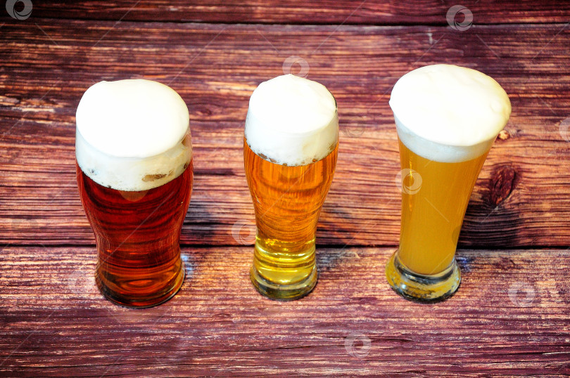 Скачать На деревянном столе в ряд стоят три бокала с разными сортами светлого пива. фотосток Ozero