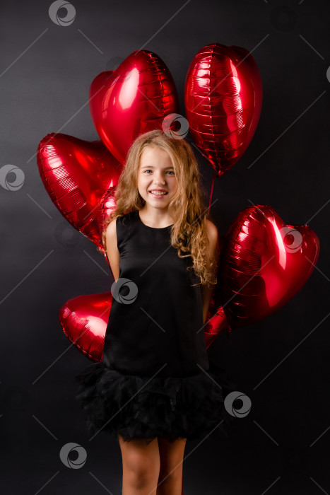 Скачать маленькая девочка с воздушными шариками в форме сердца посылает воздушный поцелуй на черном фоне. Концепция Дня святого Валентина фотосток Ozero