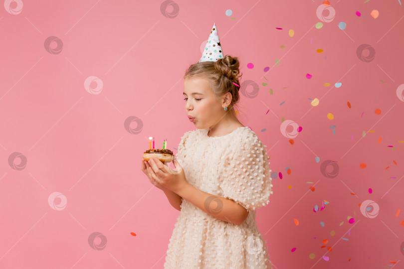 Скачать Счастливая маленькая девочка в шапочке на свой день рождения загадывает желание и задувает свечи на торте. Розовый фон, текстовое пространство фотосток Ozero