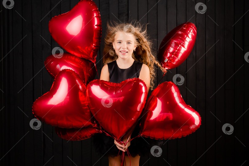 Скачать маленькая девочка с воздушными шариками в форме сердца посылает воздушный поцелуй на черном фоне. Концепция Дня святого Валентина фотосток Ozero