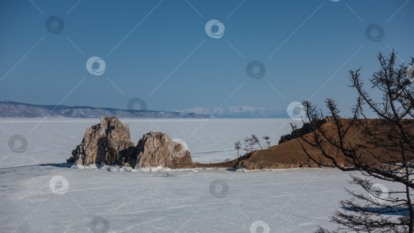 Скачать Необычная живописная двуглавая скала возвышается над озером, покрытым льдом и снегом. фотосток Ozero