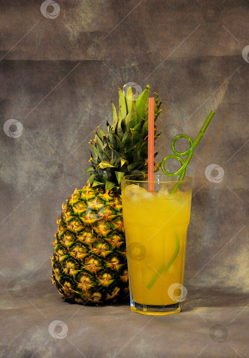 Скачать Высокий бокал желтого нектара со льдом и спелым ценным ананасом на сером фоне. фотосток Ozero
